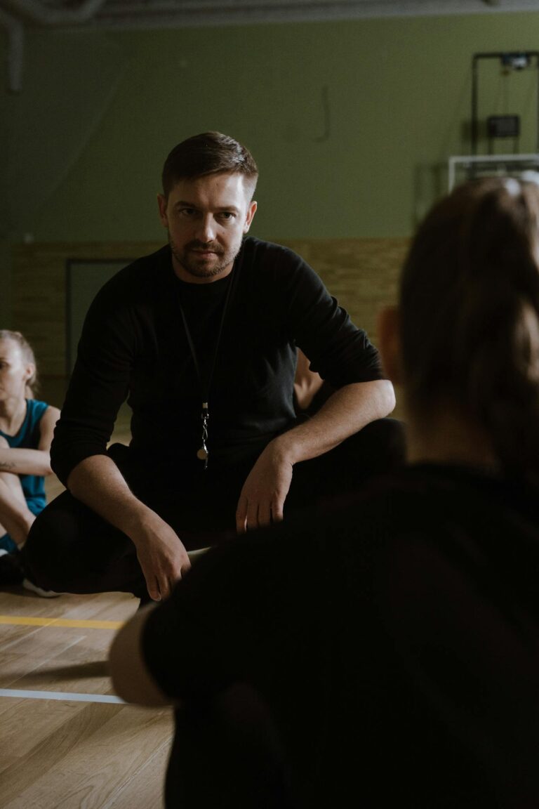 Basketball coach giving instructions to players in an indoor court setting.